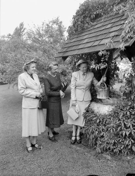 Garden show and tea at which the West Side Garden club entertained other garden clubs of the Madison area.  Mrs. T.M. Gordon, left, Ruth E. (Mrs. Arthur) Towell, middle, and Nora (Mrs. S.L.) Rorge, right, admiring the wishing well in the garden at 2310 Gilbert Road.