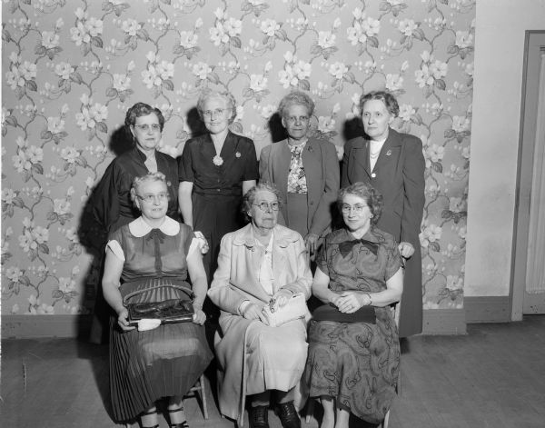 Group portrait of charter members of the Madison Veterans of Foreign War, who are observing the organization's 25th anniversary.  Front row, left to right: Bertha Podhaler, Helen Lang, and Christine Kohlman. Back row: Louise Turner, Jessie Holmes, Susan Miller, and Ruth Church.