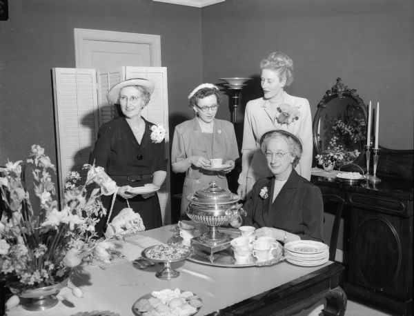 Representatives of three organizations belonging to the Women's Auxiliary of Madison General Hospital are shown at the tea table with their hostess at the auxiliary's spring tea and garden party. Standing, left to right: Caryl Gay, American Business and Professional Women's  Club; Kathryn Davis, Soroptimist; and Dr. Ethelred Schafer, Zonta. Seated is the hostess, Louise Brown, wife of Supreme Court Justice, Hon. Timothy Brown.