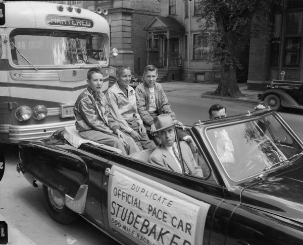 Three newspaper carriers riding in Studebaker duplicate of the official pace car for the Indianapolis 500 mile race in front of the buses that took one hundred eighteen newspaper carriers to see the race.