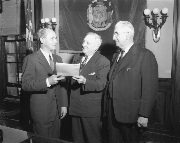 Lew Wallace, Vice-President of the National Safety Council, center, is shown giving a safety award to R.C. Salisbury, left, chief of the Motor Vehicle Department highway safety promotion division. Governor Walter Kohler is standing on the right.