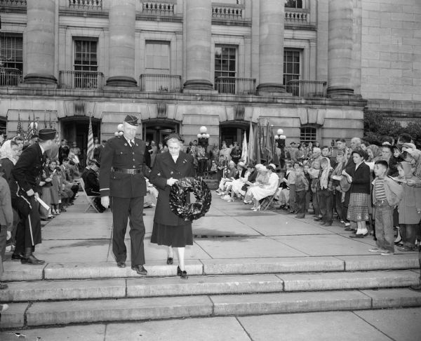 Mrs. H.L. (Charlotte) Gerber, escorted by Earl Heath, prepares to place a wreath in honor of World War I dead during ceremonies at the South Hamilton Street entrance to the Wisconsin State Capitol.
