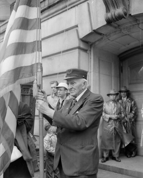 Eighty-two-year-old William N. Nichols holding a flag during Memorial Day services at the Wisconsin State Capitol. He is the son of a Union Civil War veteran and he served with the Pennsylvania militia in 1892.