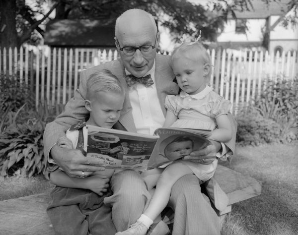 Grandfather Harry L. Geisler reads a Woman's Day magazine to his grandchildren, Timmy (James William), 5, and Nancy Anne, 2, at their home at 3120 Oxford Road. The photograph was part of a newspaper feature on fathers and their children.