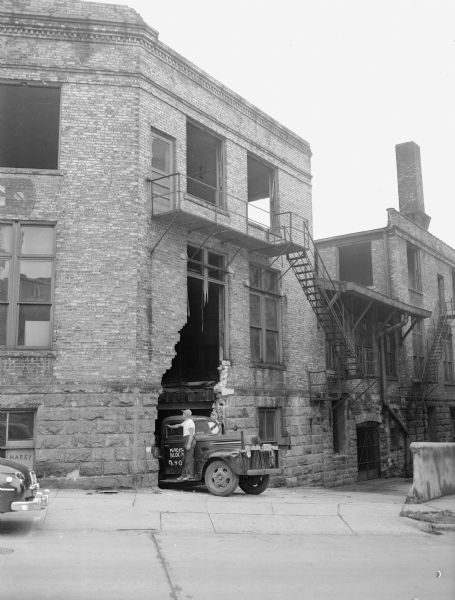 Carl Federman, foreman of the Allen Wrecking Company, standing on the truck being loaded with debris from the razing of the Democrat Printing Company building at the corner of S. Carroll and W. Doty streets, a building that had been at this location since 1890.