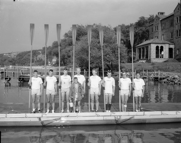 The University of Wisconsin varsity crew posing on a pier prior to leaving for the Intercollegiate Rowing Association regatta in Syracuse, New York. The coxswain, standing in front, is Don Rose of Ft. Atkinson. Oarsmen, left to right, are: Robert Nelson, Edgerton; James Lorenzen, Wisconsin Dells; Robert Espeseth, Cameron; James Moran, Madison; Victor Steuck, Oshkosh; James Schmidt, Wauwatosa; Robert Hood, North Prairie; and Delos Barrett, Lannon.