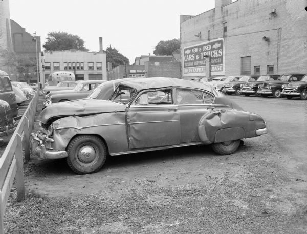 Damaged automobile sitting on the lot at Hult's Capital Garage, 608 E. Washington Ave. with Thomas Olson Auto Accessories, 609 E. Washington Ave. and Mautz Paint Store, 615 E. Washington Ave. visible across the street.  Photo was taken for Attorney Farrand Shuttleworth.