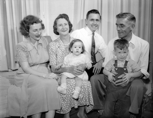 Mrs. Mary Ellen Fletcher used an inheritance to fly her mother and father in-laws from Birmingham, England to Madison to witness their sons graduation from mechanical engineering school at the University of Wisconsin. The family is shown seated, left to right, they are: Mary Ellen Fletcher, Mrs. Arthur James Fletcher with 10-month-old granddaughter Valerie, their son, Norman and Mr. Arthur James Fletcher with grandson Gregory, 2 years-old. Norman Fletcher was a "war groom" and British air combat veteran. Mary Ellen Fletcher was a WAVE in Florida, where she was a trainer instructor, and where they met in 1944.
