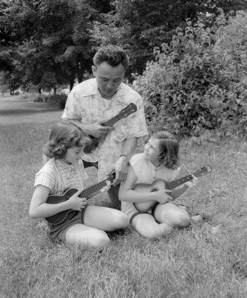 Dick Miyagawa, recreation director and supervisor of the summer Shorewood Hills Play School, gives pointers on playing a ukelele to Lucina Meloy, left, and Judy Lang.