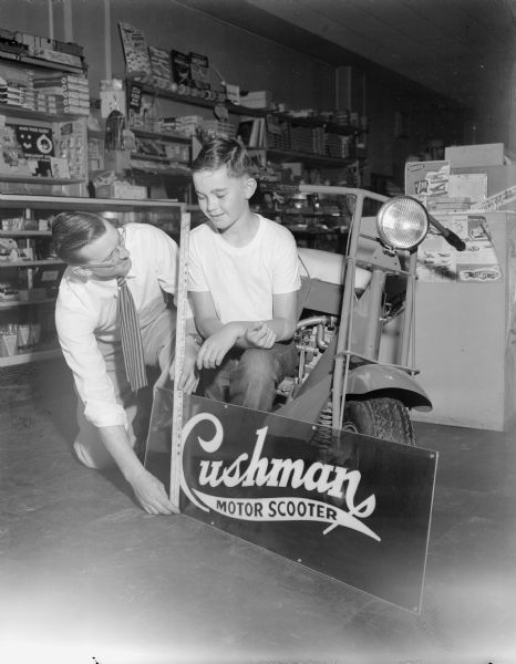 Al Decker, manager of Cushman Hobbyland at 2628 University Avenue, and Johnny Schaffer measure a sign for the company to see if it will fit on the racer the company is sponsoring in the soap box derby to be driven by Johnny.
