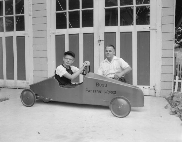 Alvin Boss, owner of Boss Pattern and Model Works, poses with his son Dick who is seated in the soap box derby racer he will race in the upcoming race.