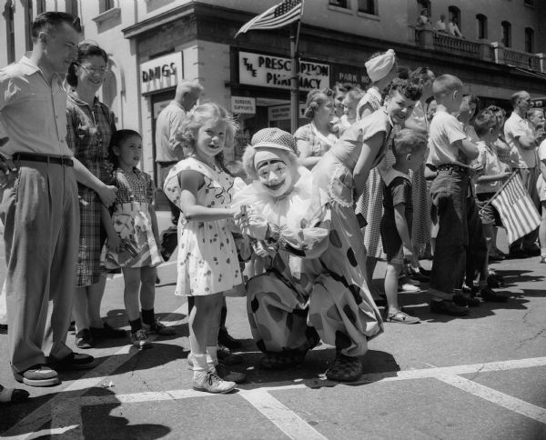 A clown in the Fourth of July parade sponsored by the East Side Business Men's Association (ESBMA) helps a young girl open her package of candy. The girl is Bonnie Parker, daughter of Mr. and Mrs. Robert Parker, 1812 Keyes Avenue.