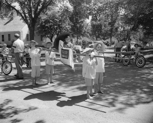 Four girls costumed as Chinese 'coolies' carry a fifth girl seated up in a sedan chair. They are, left to right: Jean Verthein, Darlene Conner, Cindy Wheeler in the chair, Clarice Conner and Ellen Wheeler.