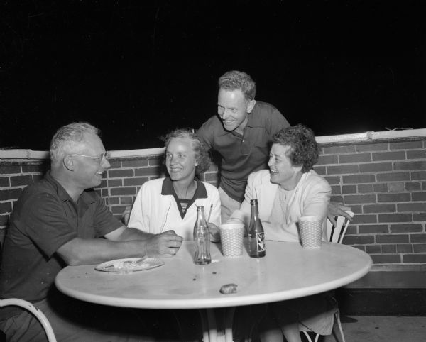 From left, Benjamin Huiskamp, Evelyn Aitken, Donald Aitken (standing), and Janet Huiskamp at a table during the Mendota Yacht club Moonlight Regatta and picnic supper on the roof of the Edgewater Hotel.
