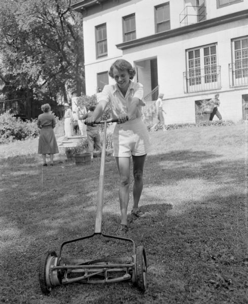 Attic Angel members (plus a few husbands and children) took part in a clean-up party at the former Louis M. Hobbins house at 102 East Gorham Street that the association had purchased for a nursing home. Margaret Stroud, a probationary Attic Angel member, mows the lawn.