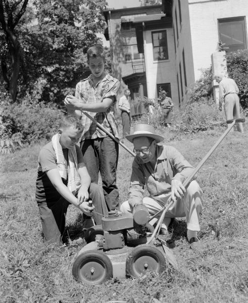 Attic Angel members (plus a few husbands and children) took part in a clean-up party at the former Louis M. Hobbins house at 102 East Gorham Street that the association had purchased for a nursing home. William H. Purnell, whose wife is the clean-up day chairman, is shown giving instructions on the operation of a power mower to his son, Tony, who is kneeling at the left. Looking on is Tim Dean, the son of Dr. and Mrs. Joseph C. Dean.