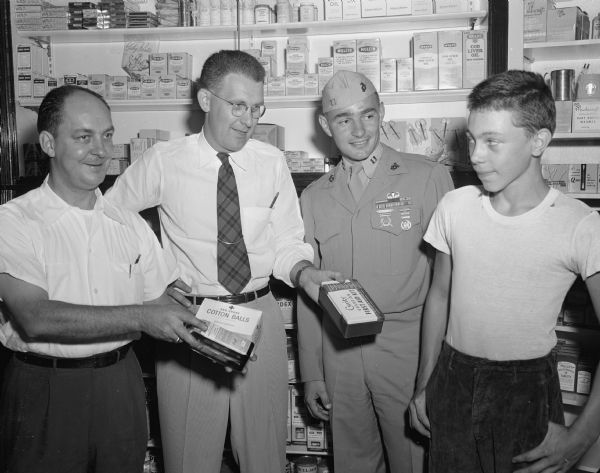Carlos Bast (right) stands with representatives of his two sponsors for the Madison Soap Box Derby. J.J. Werner and Jack Meyers of Prescription Pharmacy offer Carlos first aid equipment to carry in his racer while Captain Leo Lewis of the Madison Marine Reserve Unit looks on.