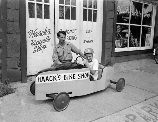 Fifteen-year old Jerry Stockland, son of Mr. and Mrs. Albert A. (Marilla) Stockland of 520 Christianson Avenue, is shown sitting in his racer with proud sponsor, Frank Haack of Haack's Bike Shop at 1250 East Washington Avenue. 150 Madison youth are entered in the annual race sponsored by the Wisconsin State Journal and Hult's Chevrolet.