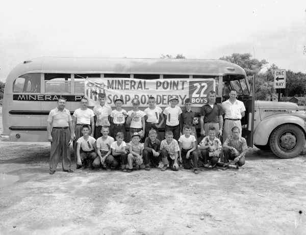 Fifteen derby boys and four adults from Mineral Point who came to Madison for the Madison Soap Box Derby are standing in front of their school bus. Larry Laverty, a 14-year-old farm boy who was crowned the champion, is the fifth from the left in the back row.