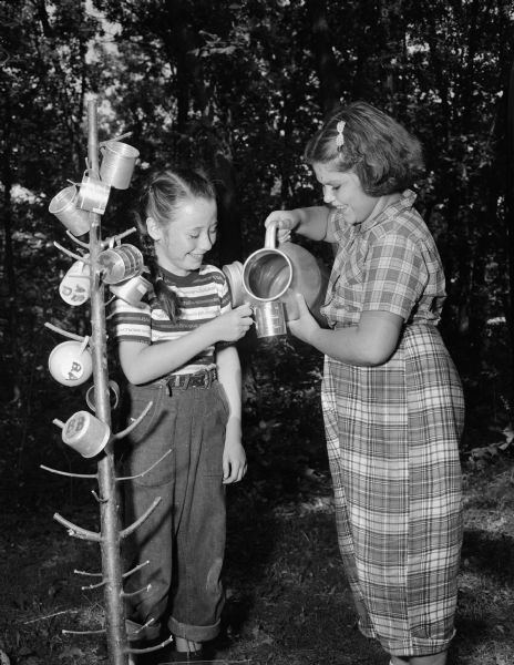 Barbara Arnett, Oregon, pours a cup of cold water for Mary Ellen Jordan, Waunakee, at the "cup tree," used at the Brownie Hoyt Park Day Camp to store campers' cups when not in use.