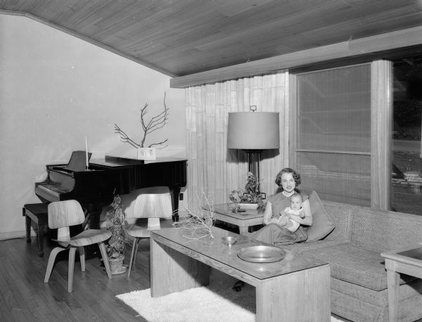 Interior view of the home of Mr. and Mrs. Don J. (Jean) Voegeli at 2805 Oxford Place in Shorewood Hills. The spacious one-story home was designed around the three young Voegeli children. The 18 by 22-foot living room, features a large picture window and a cathedral ceiling and is furnished with contemporary "child friendly" furniture. Mrs. Voegeli is shown seated on the sofa with 4 month-old Kim, the youngest of the three Voegeli children.