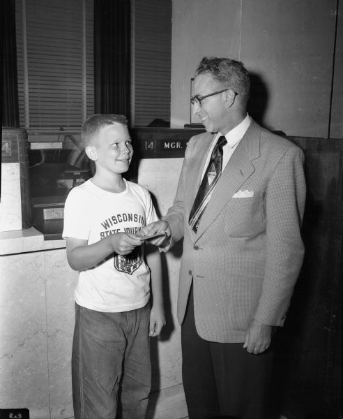 Larry Jacobson, 11-year-old Soap Box Derby racer, receives a $25 savings account from Herman J. Kneubuehl, manager of First National Bank. The bank annually makes this award to the best competitor among Madison youths entered in the derby.
