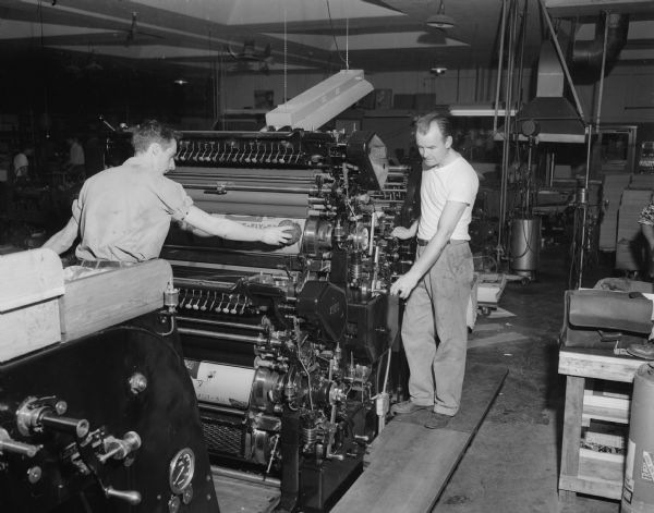 A new, two-color, lithograph press, capable of running off over 7,000 impressions an hour with color perfectly registered, is examined by Walter Larson (left), pressman helper, and Kenneth Voss, head pressman of Straus Creative Printers and Lithographers, 1028 East Washington Avenue.