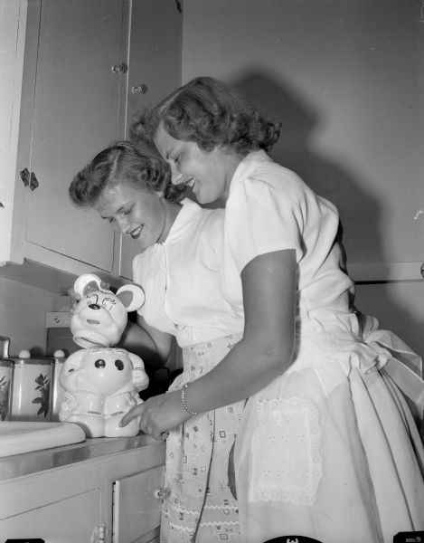 Softball players and twins Darlene and Arlene Bates are shown in their apartment 'robbing' their cookie jar. They both worked at Oscar Mayer and Co. doing clerical work.