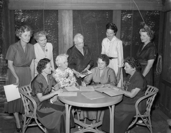 Members of the Madison Civic Club board sitting around a table. They are, left to right: Margaret Uhl, treasurer; Mrs. A.H. Edgerton, social chairman; Naomi Price, secretary. Standing left to right: Frances Kivlin assistant social chairman: Gertrude Lamb, past chairman; Charlotte Wood; Sara Johnson, vice chairman; and Evelyn Wheeler, assistant secretary.