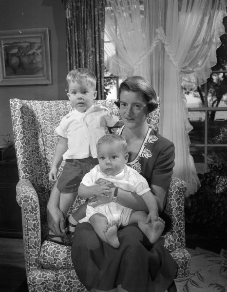 Family portrait of Mrs. Jack (Mary) Tausend and her two young sons, Wellwood, 20 months (standing), and Marc, 7 months, seated on his mother's lap. Mrs. Tausend (the former Mary Nesbit) and her children are visiting her father, Dr. Wellwood Nesbit, 25 Fuller Drive. The Tausends live in Houston where her husband is a doctor.