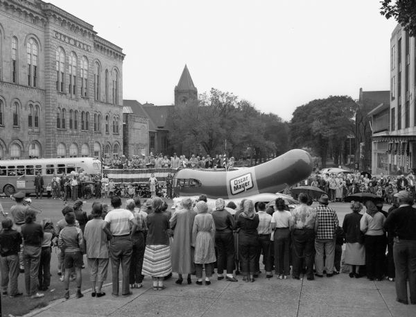 The Oscar Mayer Wienermobile passes by spectators watching the Labor Day parade on Capitol Square. City Hall is visible in the background.