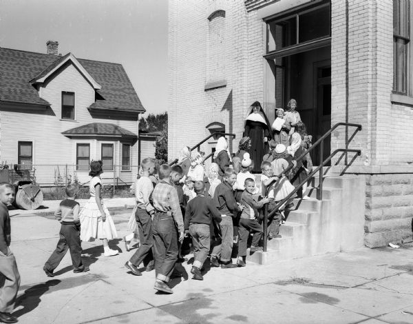 A group of students are shown 'trudging' up the steps at St. James school as Sister Mary Ferdinella, principal, welcomes her flock from atop the steps.