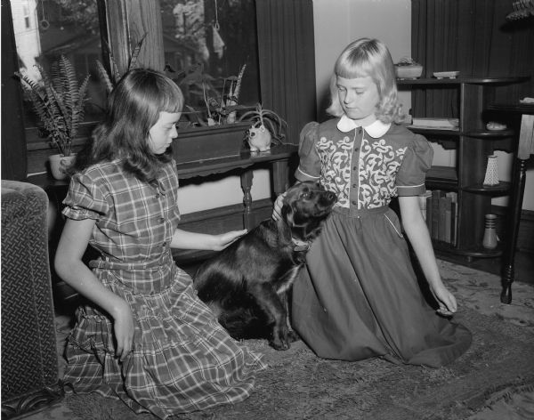 Joellen and Jean Schroeder kneeling on the floor beside their dog, Brownie, during National Dog Week.