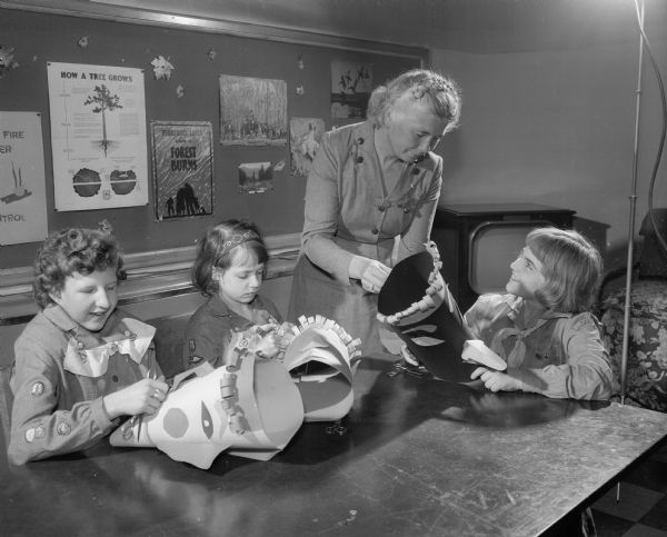 Three members of a Girl Scout troop at the Washington Orthopedic school, and their leader and teacher, Miss Erna E. Schweppe, are shown making hats for a Halloween party as part of the Girl Scout Week celebrations. Pictured left to right are Darlene Lochner, daughter of Mr. and Mrs. Leonard Lochner; Marian McElmurry, daughter of Mr. and Mrs. C.A. McElmurry; and Kathryn Grise, daughter of Mr. and Mrs. Walter Walker.
