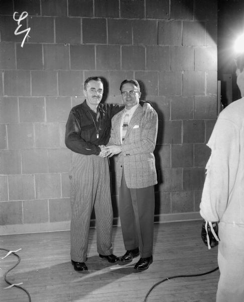 A man, probably boxing coach John Walsh, shaking hands with another man. A man is standing with his back to the camera in the right foreground.