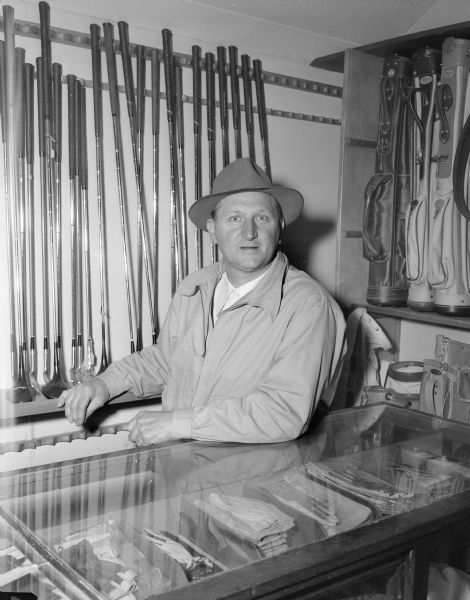 George Vitense, Nakoma golf course profession, poses behind a counter where golf clubs and supplies are displayed.