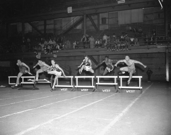 Six male students participate in a low hurdles race.