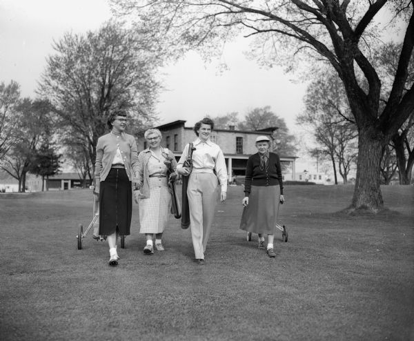 Four members of the Women's Municipal Golf Association strolling along the Monona Golf Course.  Left to right: Dorothy Webber, Gladys Marshall, Nina Richards and Barbara Torkelson. In the background is the Monona Golf Course clubhouse, now known as the Nathaniel Dean House, 4718 Monona Drive.