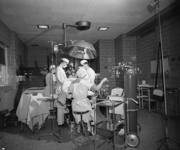 View of a surgical procedure in process at Madison General Hospital. Student nurses are observing from a glassed-in gallery at the rear.