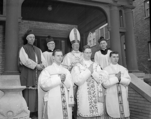 Three new priests who were ordained in Holy Redeemer Catholic Church for the Diocese of Madison pose outdoors on a staircase. They are, in the front row from left: Rev. Thomas Massion, Chicago; Rev. August Buenzli, Madison; and Rev. James McEnery, Chicago. In the back row are, left to right: Rt. Rev. Msgr. Edward M. Kinney, rector of St. Raphael Cathedral; the Rev. Joseph Gabriels, pastor of Holy Redeemer, Bishop William P. O'Connor, and Very Rev. Jerome Hastrich, chancellor of the Madison diocese.