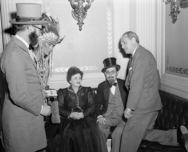Governor Walter Kohler (right) visiting with four members in period costume (a woman, a man dressed as an Indian, and two members of the Brothers of the Brush) at the Capitol building. They are part of a delegation from Prairie du Chien who are in Madison to publicize the opening celebration of the Villa Louis.