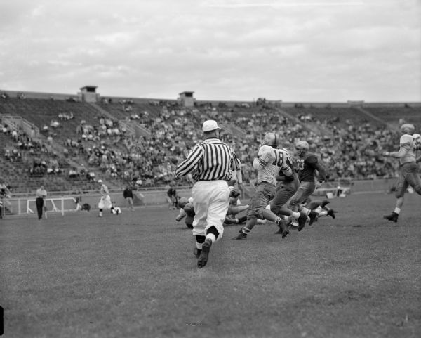 Action in the spring football game for the University of Wisconsin at Camp Randall stadium. Players shown are Captain Roger Dornbury (#18) and Clarence Stensby (#33). A referee is in the foreground.