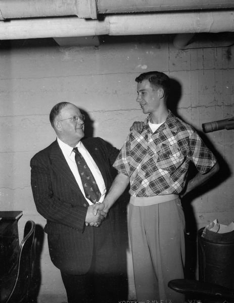 Clarence Beebe, director of the Four Lakes Drum and Bugle Corps of Madison, left, shakes hands with his "adopted Austrian son", Otto Kral.  Kral has been living in the Beebe home since 1950, and with Beebe's help has been able to attend U.W. They met through their involvement in Boy Scouting.