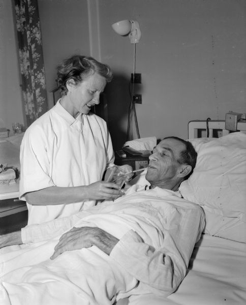 Etti Gelan, a nurse's aide at Methodist Hospital, giving a drink of water to a male patient, William Laerk of Waukesha. She left her native country of Germany to escape the Nazi regime and was a star actress and dancer in Italy before coming to America to start a new life.
