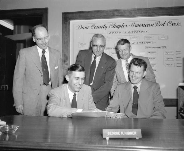 Group portrait of men planning a blood drive for Madison industrial plants at the Dane County Red Cross. Sitting are: Phillip C. Stark (left) and Bob George. Standing, left to right, are: Lucian Schlimgen, Jr., John Wrage, and Jack Thurman.