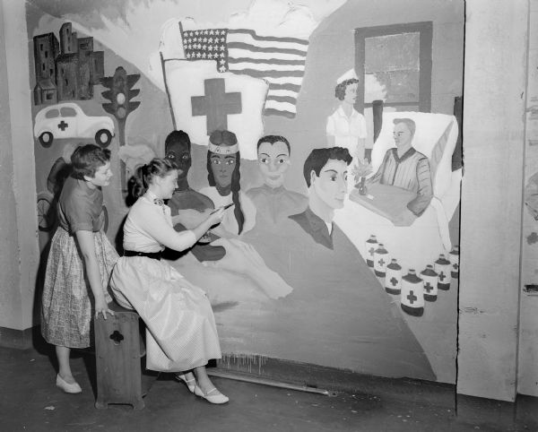 Rhoda Smith (left) and Ardele Kingeter of West Senior High School put the final touches to their symbolic mural of the Brotherhood of Man on the east wall of the Junior Red Cross assembly room, 302 East Washington Avenue.