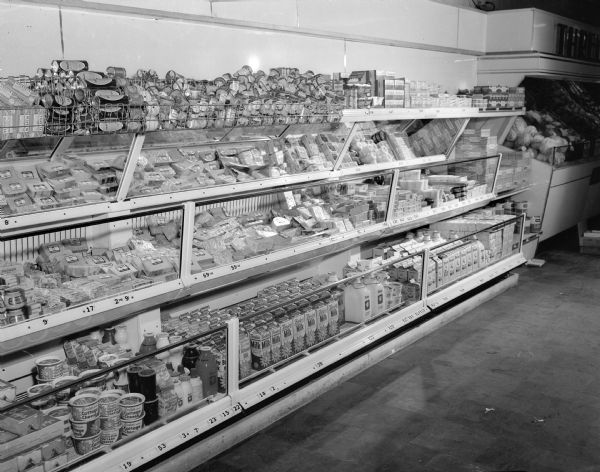 A four-level glass refrigerated display case filled with various dairy products is shown at a Piggly Wiggly store at 2701 Monroe Street. The photograph was used in a paid advertisement to commemorate June Dairy Month.