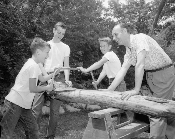 A photographic tribute to Madison Dads on Fathers' Day includes a picture of Lloyd J. Yaudes and his three sons Tommy Yaudes, John Yaudes, and Jim Yaudes sawing the trunk of a tree blown down in a windstorm earlier in the month. Lloyd Yandes is the Director of Public Relations at Wisconsin Mutual Insurance Alliance.