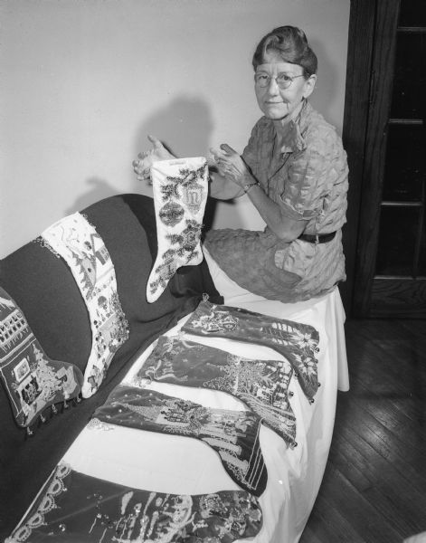 Mrs. Fred T. Cruse displays seven examples of her heavily decorated handmade velvet Christmas stockings, which she sells nation-wide and which retail for $75 to $150.