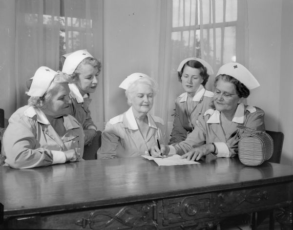 Five of the Red Cross Gray Ladies (volunteers) who work consistently at the Mendota State Hospital are shown seated around a table. Left to right, they are: Mrs. Everett W. (Frances) Rowe, Frances Stanley, Mrs. Charles A. (May) Loeffelbein, Mrs. William C. (Helen) Black, and Mrs. Claude N. (Jessie) Maurer.